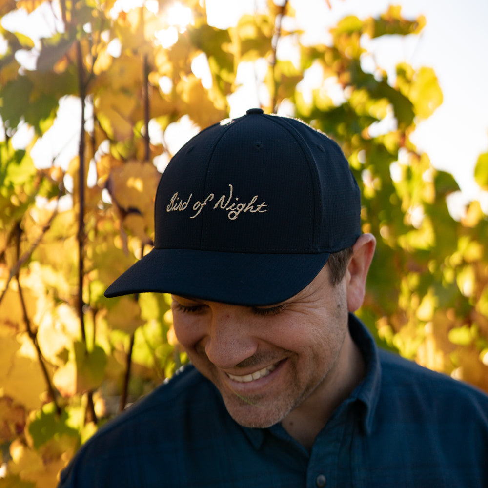 Male model wearing black Bird of Night hat in vineyard